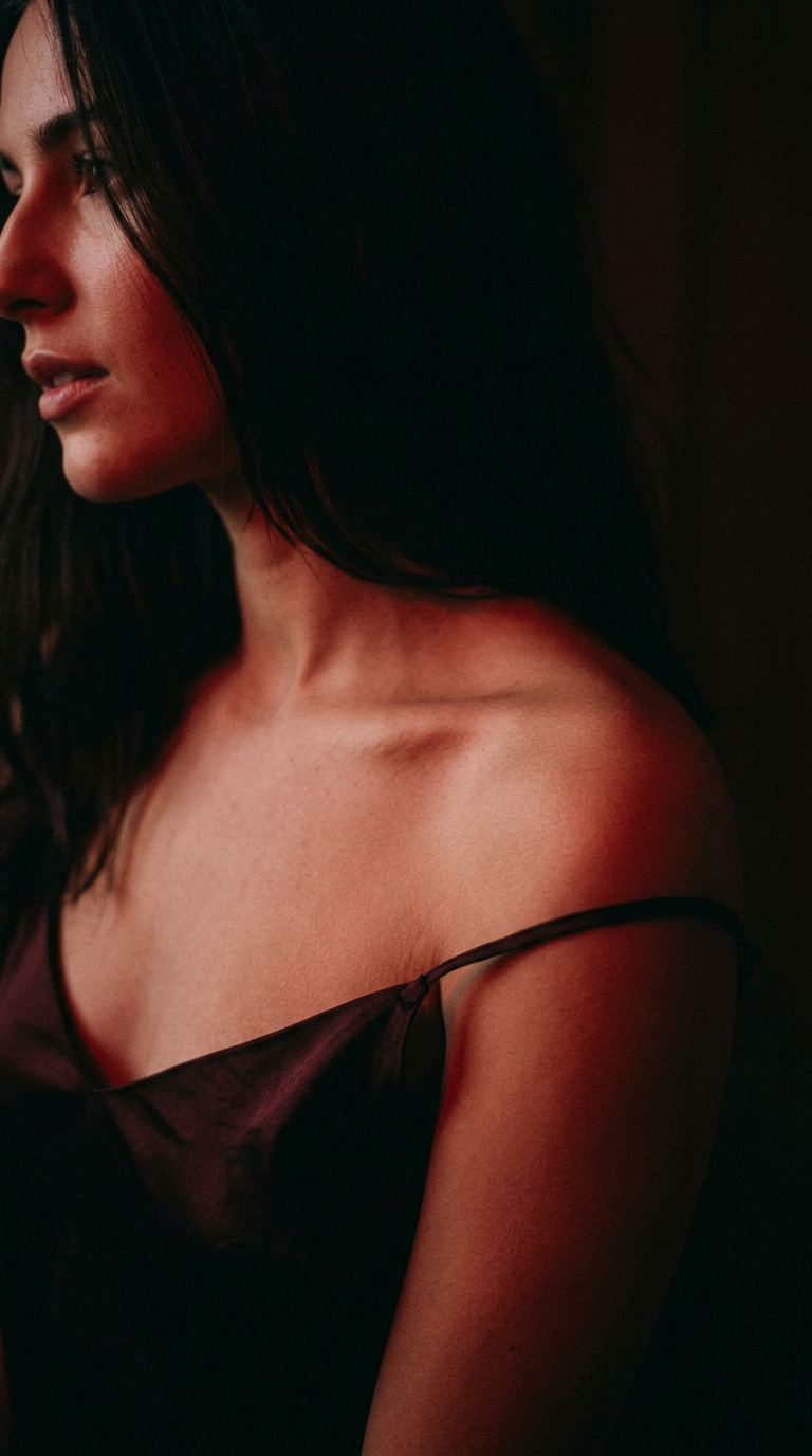 A woman in a silk slip, strap falling off her shoulder, lit by low red light